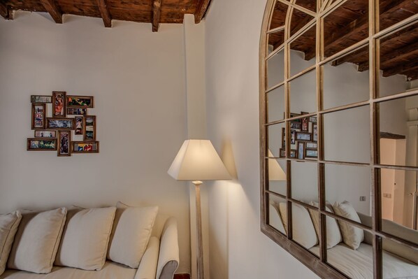 A room with a wooden ceiling, a sofa with cushions, a standing lamp, and a wall with framed pictures.