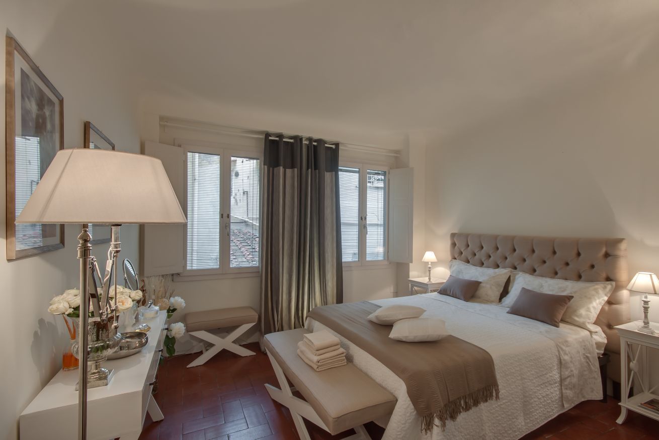 Ein Schlafzimmer mit Bett, Nachttischen, einem Schreibtisch, einer Bank und einem Fenster mit Vorhängen.