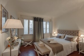 Une chambre à coucher avec un lit, des tables de chevet, un bureau, un banc et une fenêtre avec des rideaux.