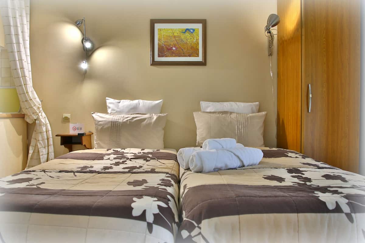 A hotel room with two beds, a wooden wardrobe, a wall-mounted lamp, and a painting.