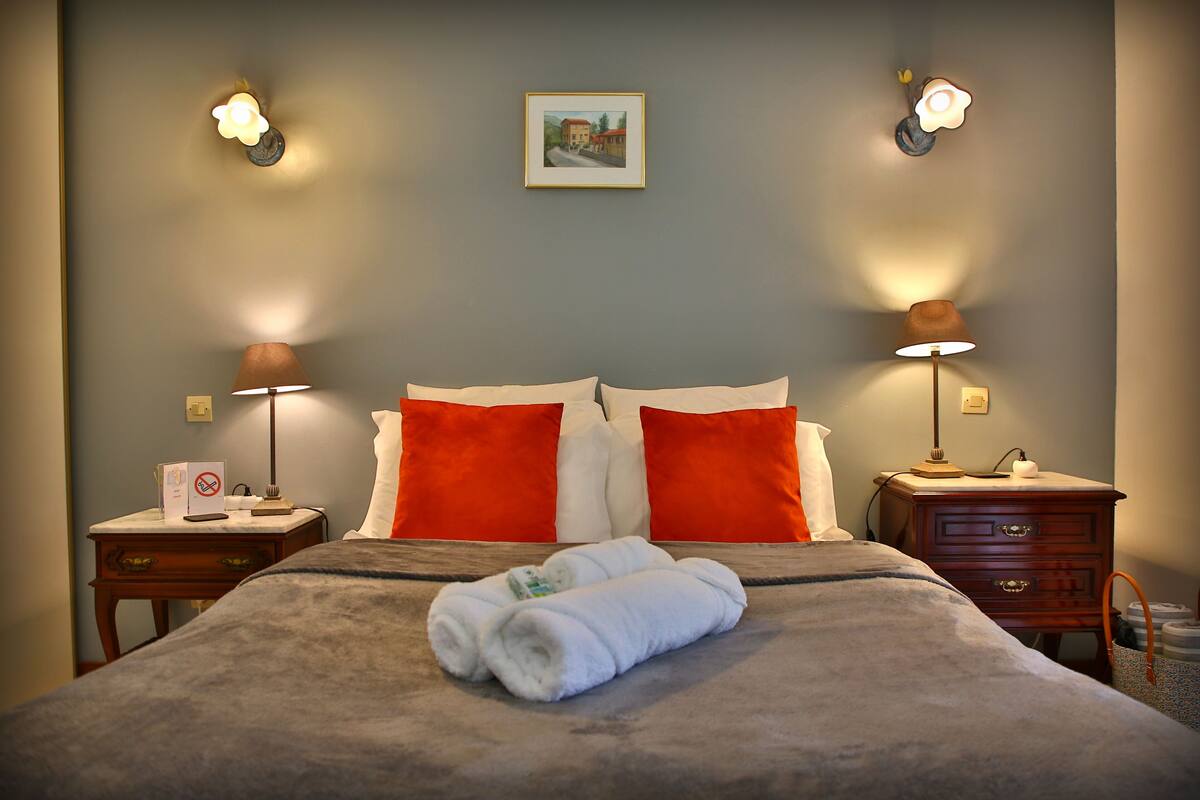 A neatly made bed with white and red pillows, two bedside lamps, and a framed picture on the wall.