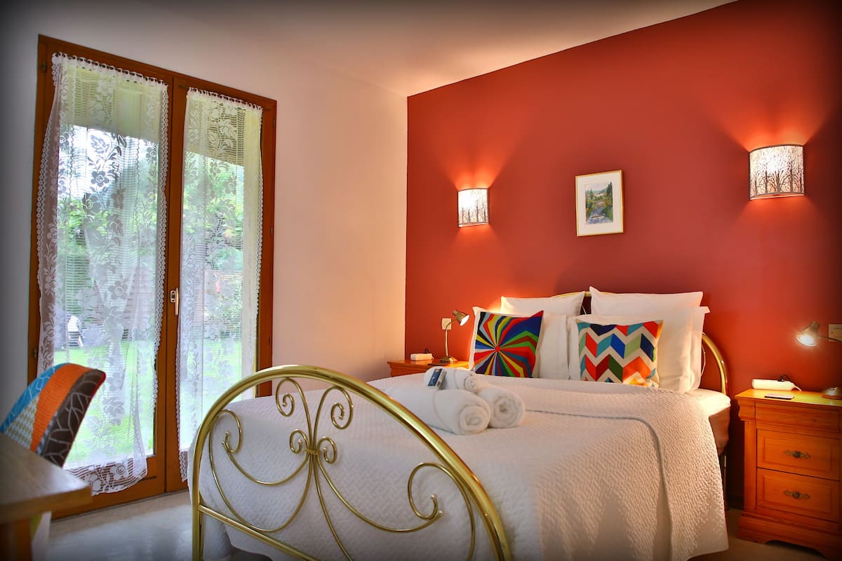A bedroom with a bed, two bedside lamps, a nightstand, and a window with curtains.