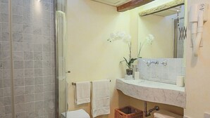 Een badkamer met een douche, een wastafel met spiegel, twee witte handdoeken, een rieten mand en een orchidee.