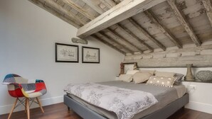 A bedroom with a bed, wooden beams, a chair, and two framed pictures on the wall. - Apartments Florence - Beautiful Terrace Serragli (Firenze)