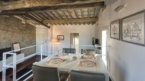 A dining area with a white table set for four, wooden beams on the ceiling, and framed architectural drawings on the wall. - Apartments Florence - Beautiful Terrace Serragli (Firenze)