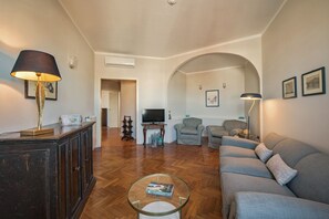 A living room with a sofa, armchairs, a coffee table, a TV, and a fireplace. - Apartments Florence - Carolina (Firenze)