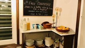 A breakfast setup with a chalkboard sign, a bowl of fruit, and various breakfast items on a counter.