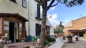 A courtyard with outdoor seating, a tree, and a building with a balcony.