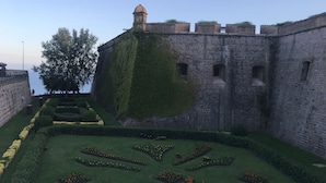 A historic stone wall with a tower, a large tree, and a formal garden with geometric flower beds.