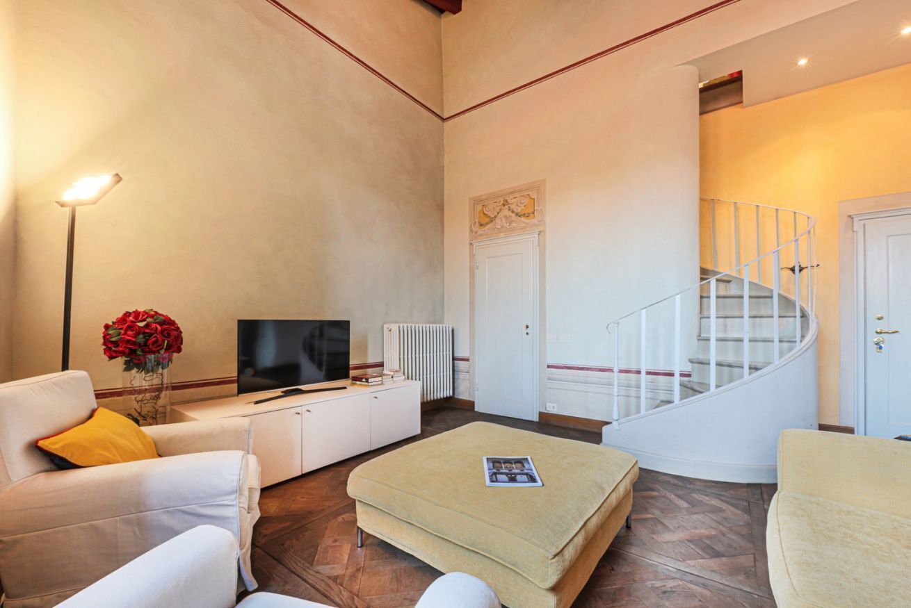 A living room with a sofa, ottoman, TV, and a staircase.