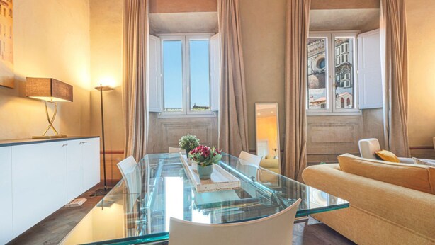 Een moderne woonkamer met een glazen eettafel, een witte bank en uitzicht op de stad door grote ramen.
