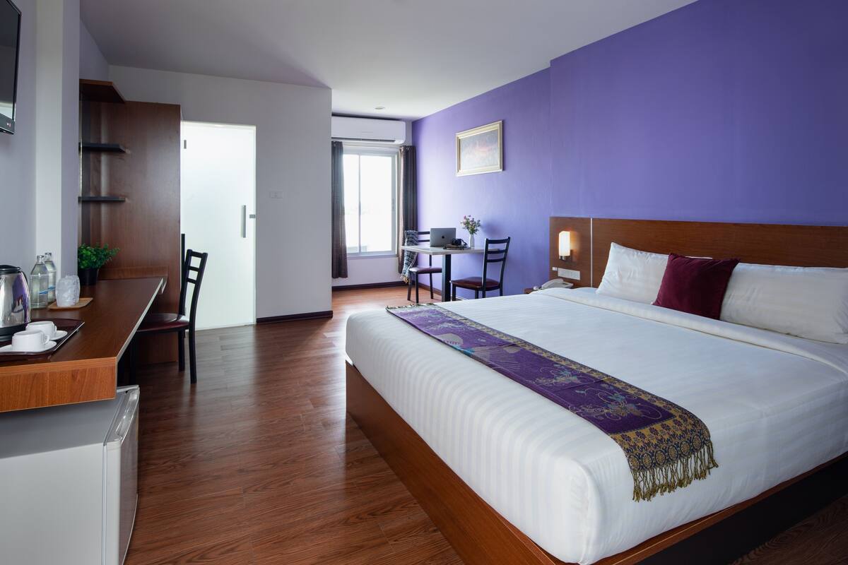 A hotel room with a large bed, a desk with a laptop, and a chair.