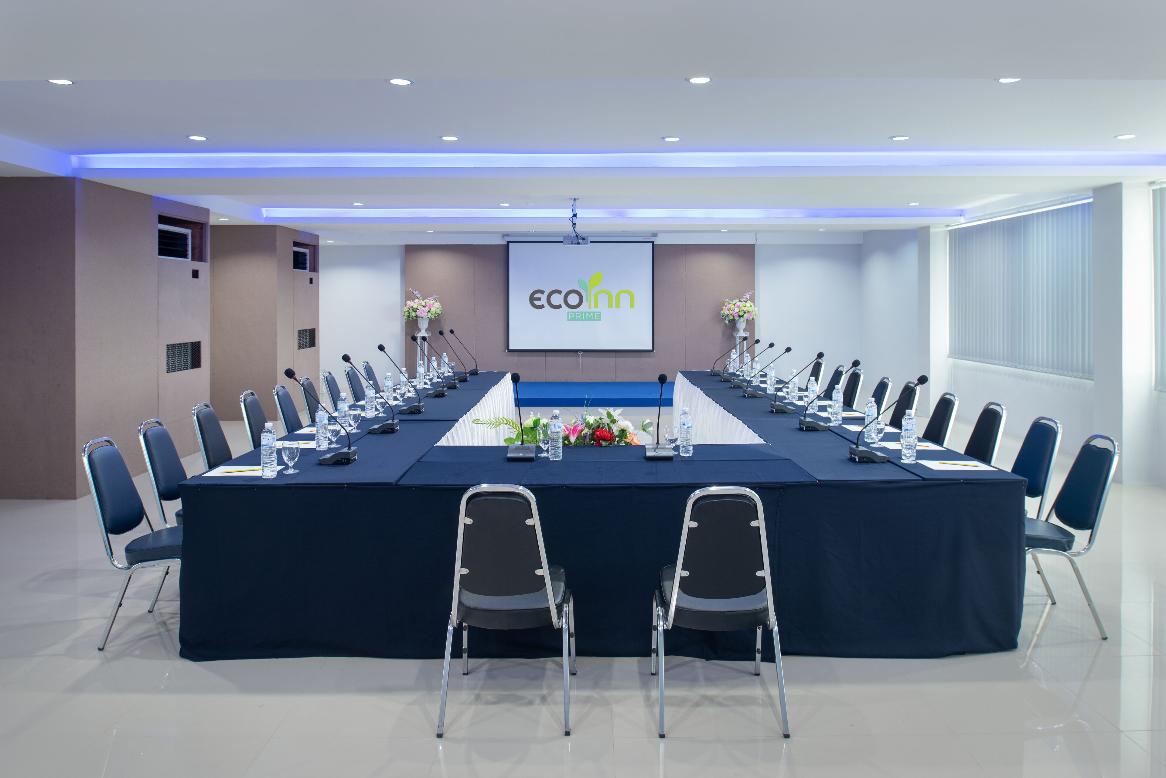Un salón de conferencias con una larga mesa, sillas, micrófonos y una pantalla que muestra el logotipo 'ecoInn PRIME'.