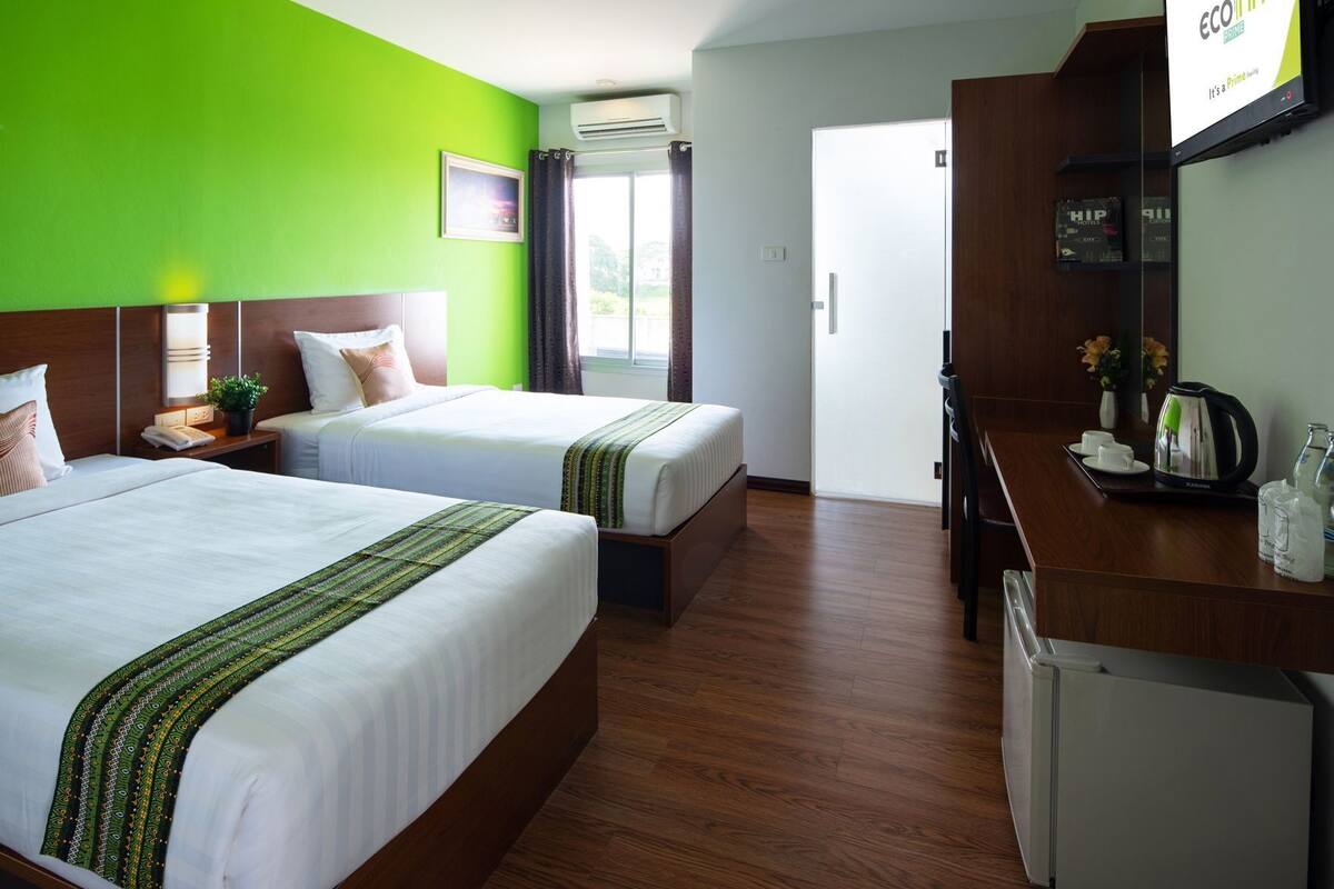 A hotel room with two beds, a desk, a coffee maker, and a refrigerator.