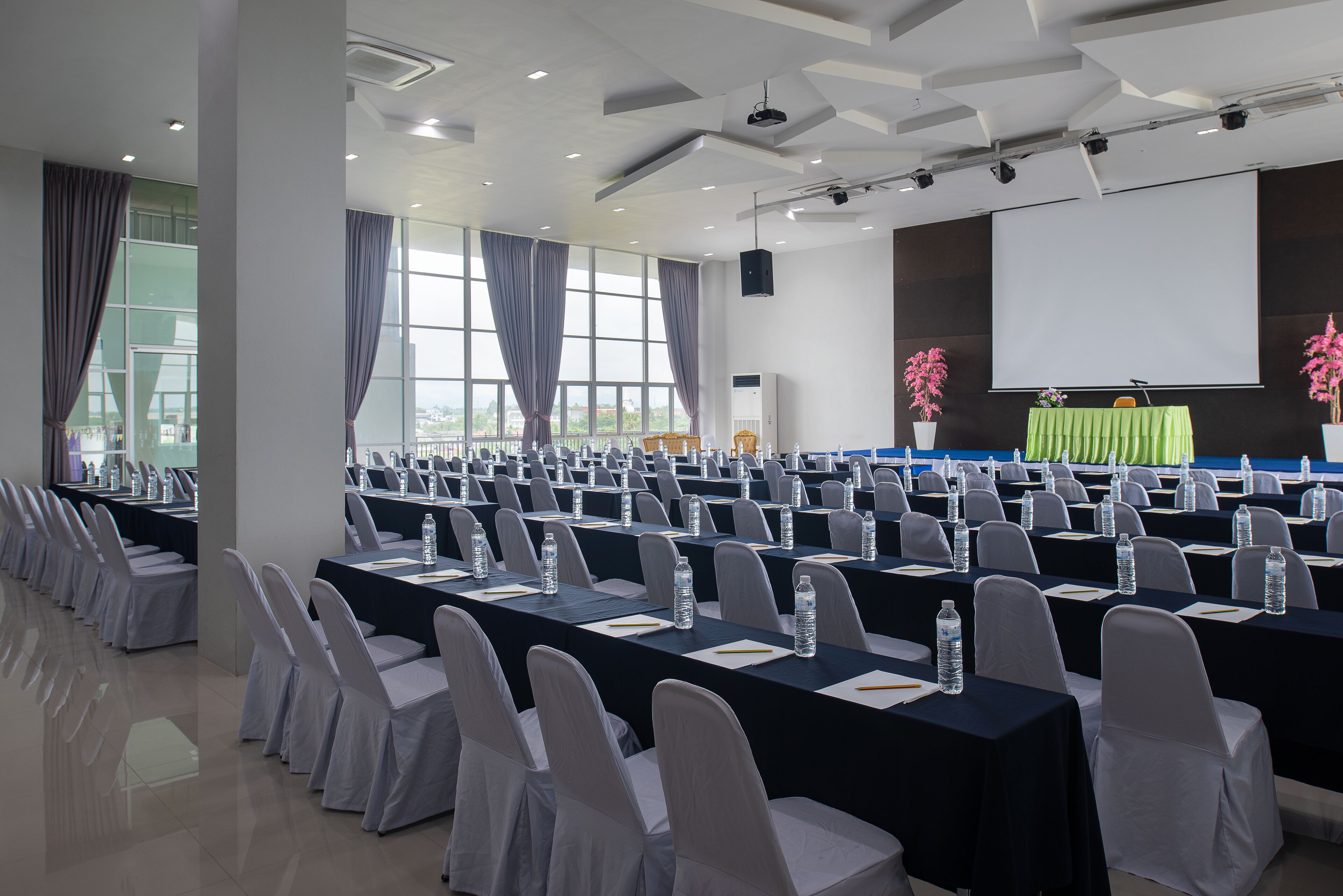A conference room with rows of tables, chairs, and a projector screen.
