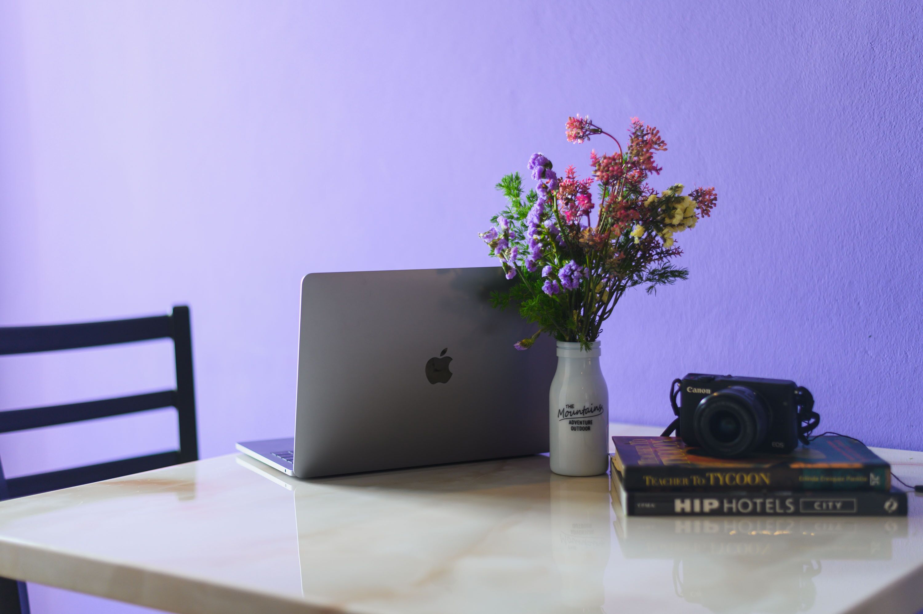 Un ordenador portátil, una cámara y un florero con flores sobre una mesa.