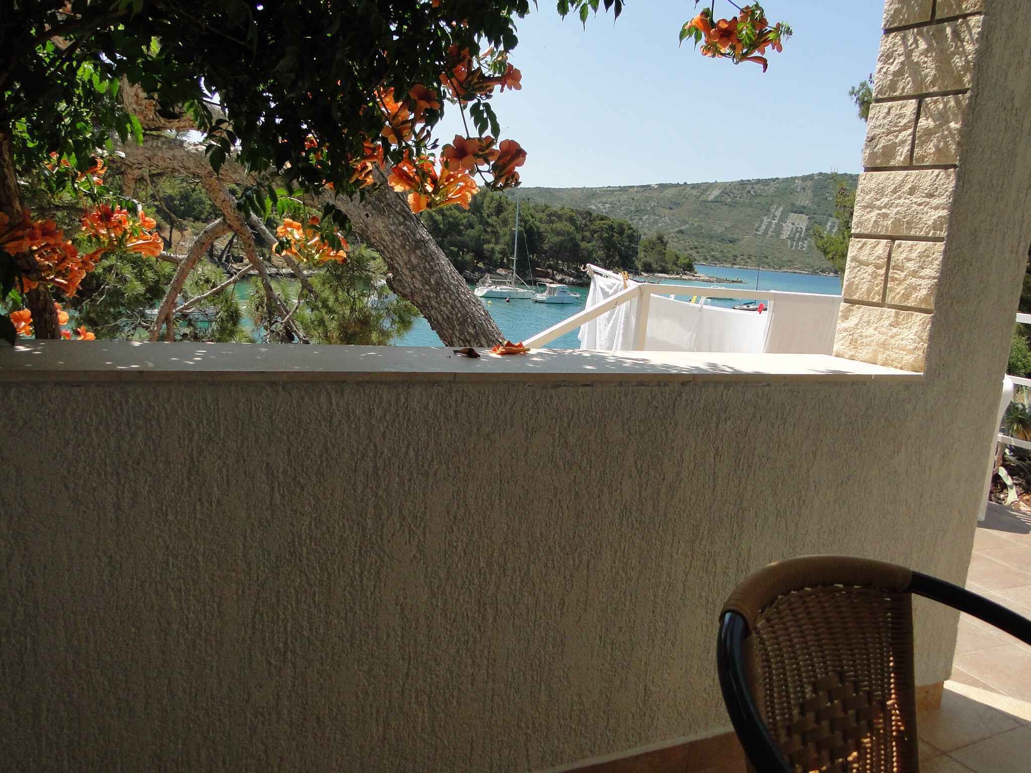 A balcony with a view of a coastal area, a wicker chair, and a white railing.