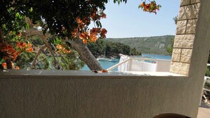 Un balcon donnant sur la côte, une chaise en osier et une balustrade blanche.