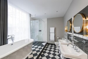 Ein modernes Badezimmer mit Schachbrettboden, einer großen Badewanne, zwei Waschbecken und einer Duschkabine.