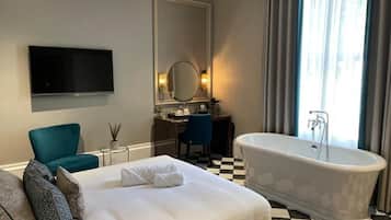 A hotel room with a large bed, a bathtub, a desk with a chair, a television, and a large mirror.