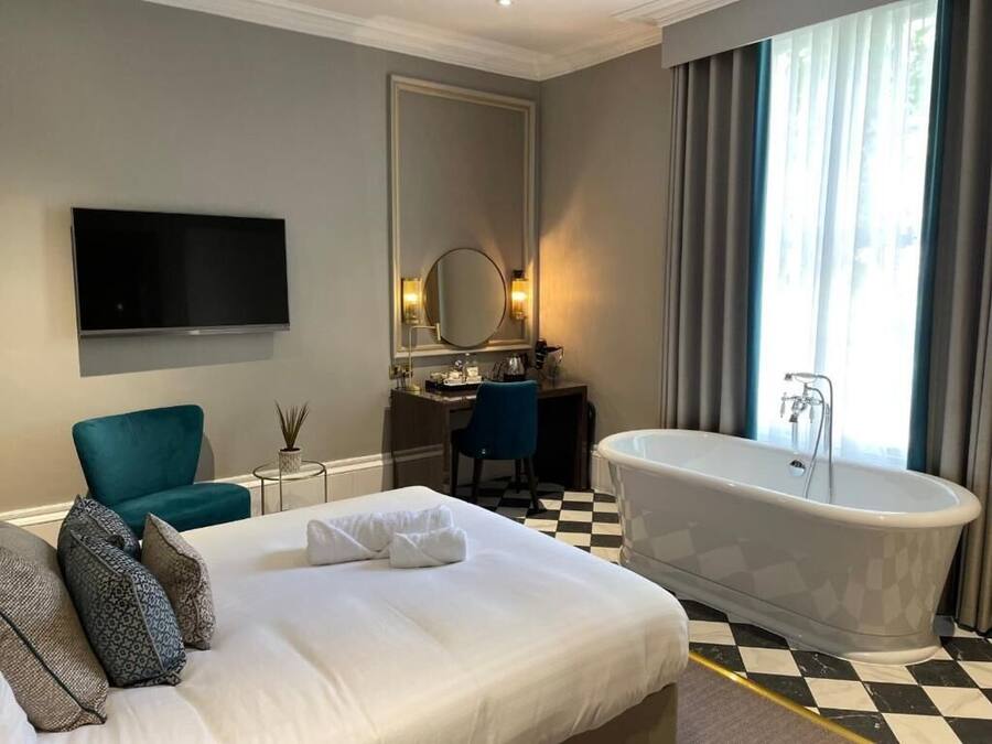 A hotel room with a large bed, a bathtub, a desk with a chair, a television, and a large mirror.