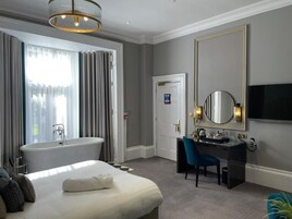 Une chambre d’hôtel avec un grand lit, un coin salon avec un bureau, une baignoire et un grand miroir.