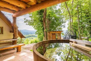 Una terraza de madera con un jacuzzi, rodeada de árboles y una vista panorámica de colinas.