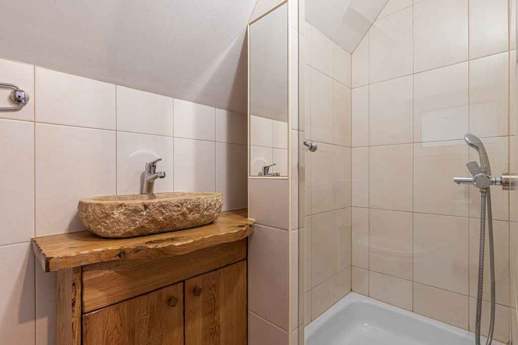 Un baño con lavamanos de piedra, mueble de madera y zona de ducha con paredes de azulejos y bañera.