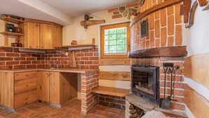 A kitchen with a brick fireplace, wooden cabinets, and a window. - Studio in the vineyards (Novo Mesto)