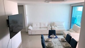 A modern living room with a white sofa set, a dining table set for four, and a large window providing a view of the outdoors. - Apartamento de Lujo Frente al Mar (Cartagena)
