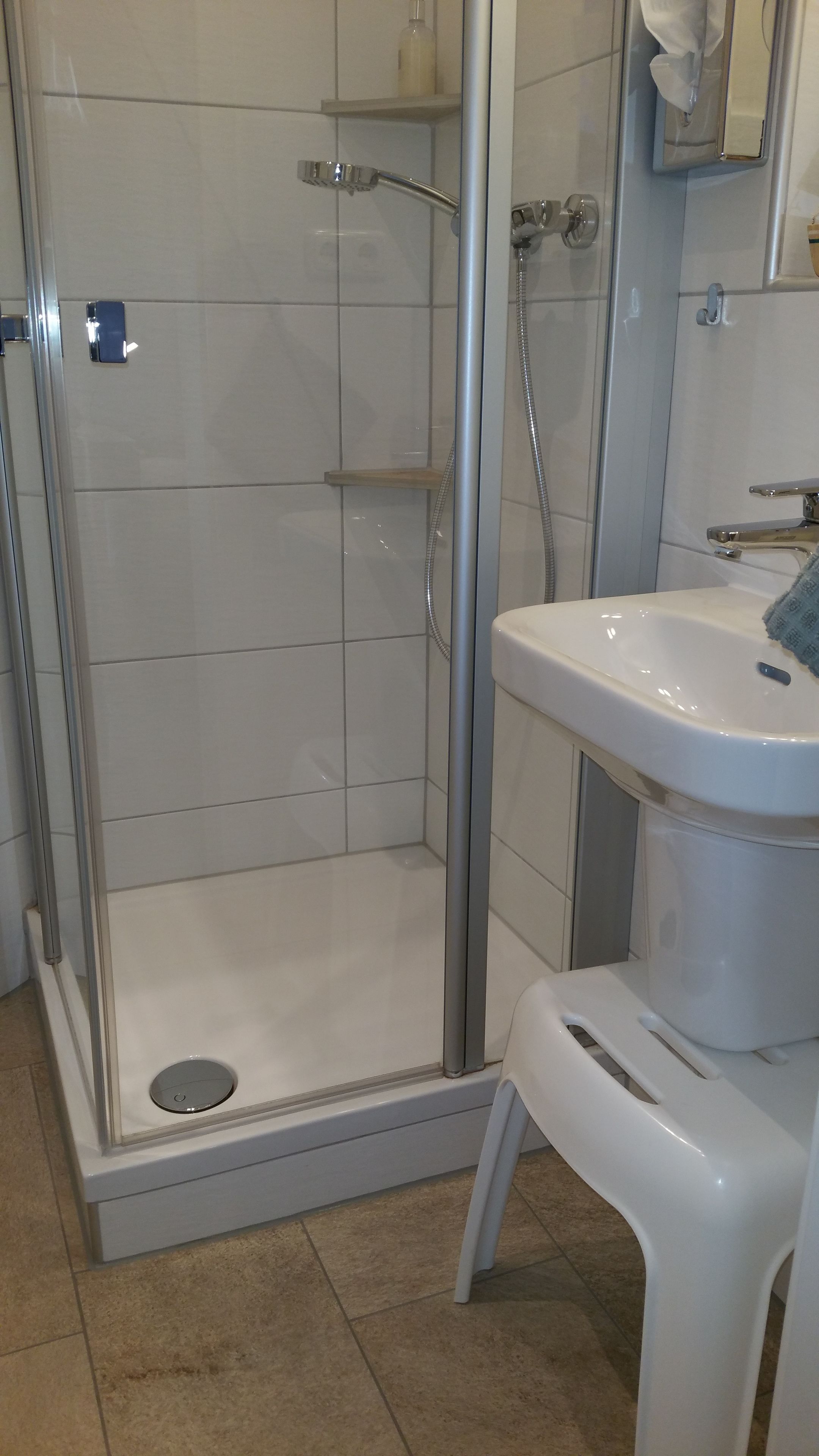 Un baño con ducha de vidrio, un lavamanos blanco y un pequeño taburete.