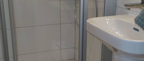 Un baño con ducha de vidrio, un lavamanos blanco y un pequeño taburete.