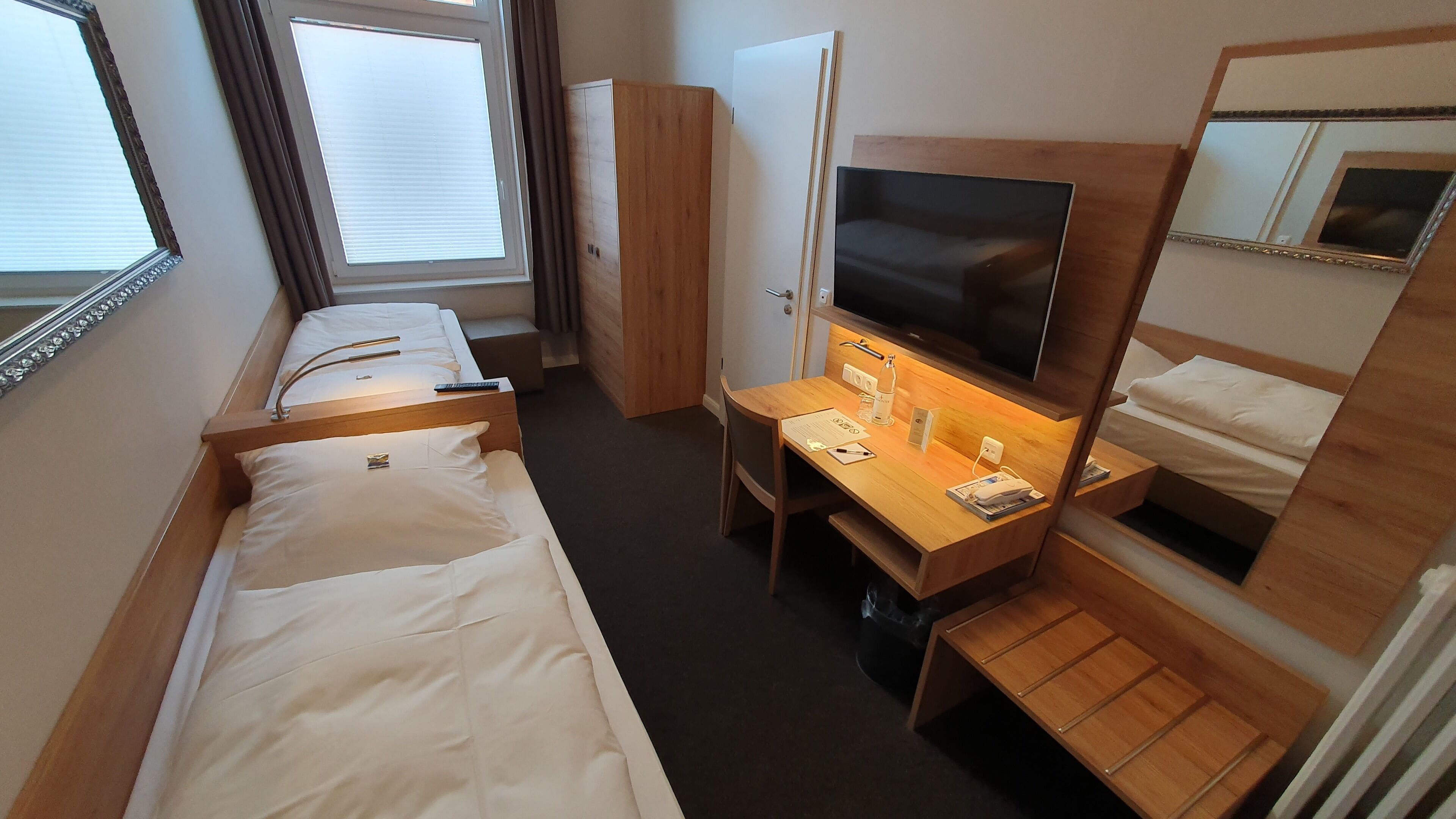 Une chambre d’hôtel avec deux lits simples, un bureau avec une télévision, un miroir et une armoire.