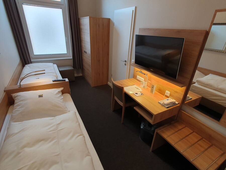 Une chambre d’hôtel avec deux lits simples, un bureau avec une télévision, un miroir et une armoire.
