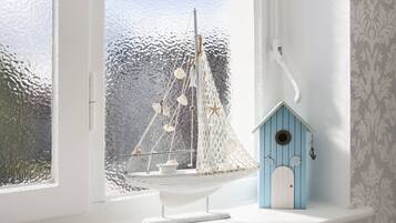 A room with a large window, a white sailboat model, and a blue birdhouse.