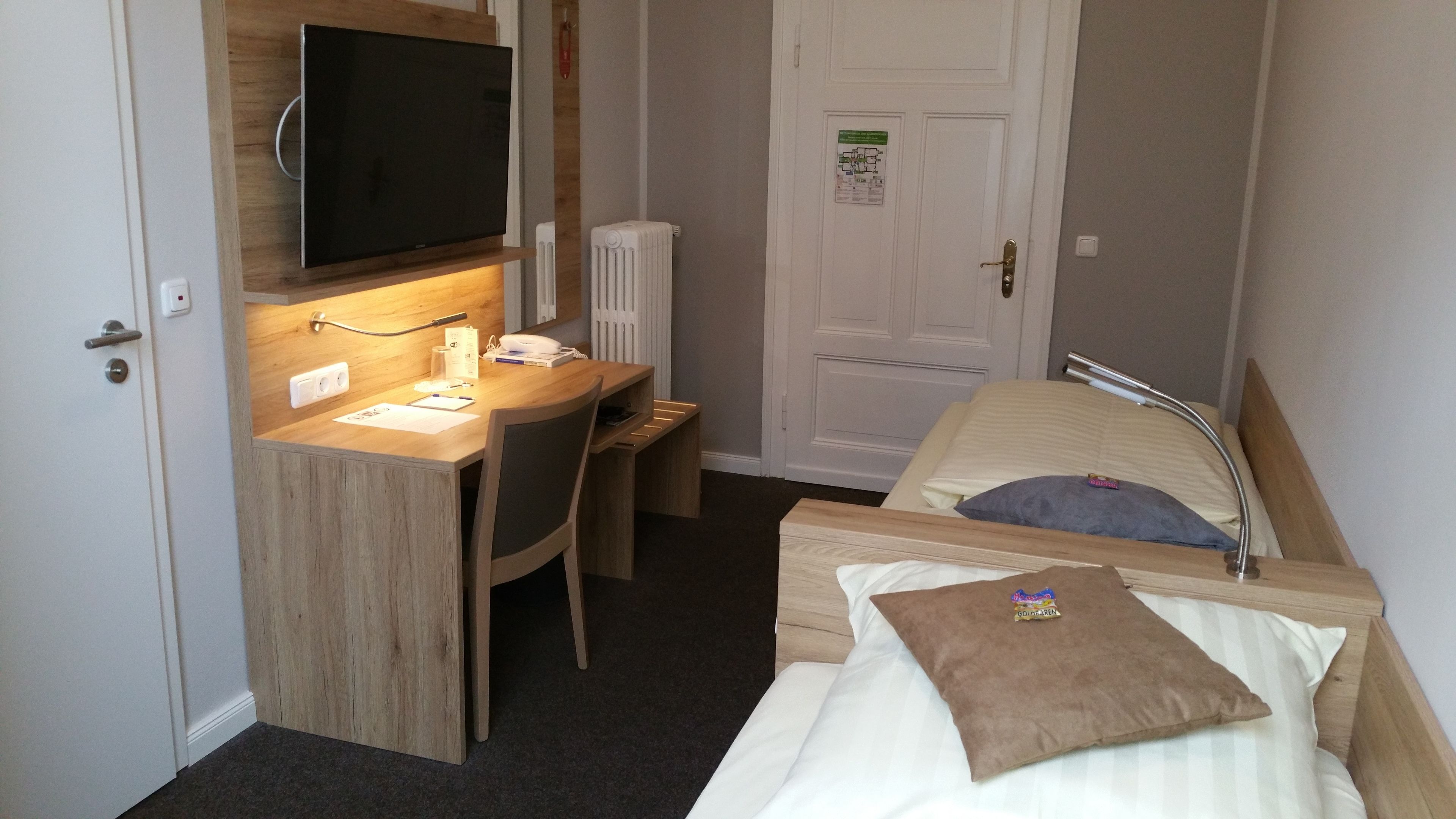 A compact hotel room with a single bed, a desk with a chair, a television, and a radiator.