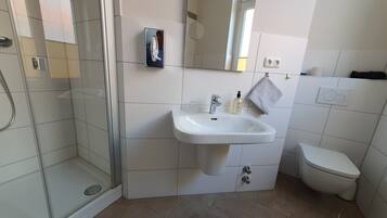 Un bany modern amb plat de dutxa de vidre, un lavabo blanc i un mirall a sobre, i un vàter.