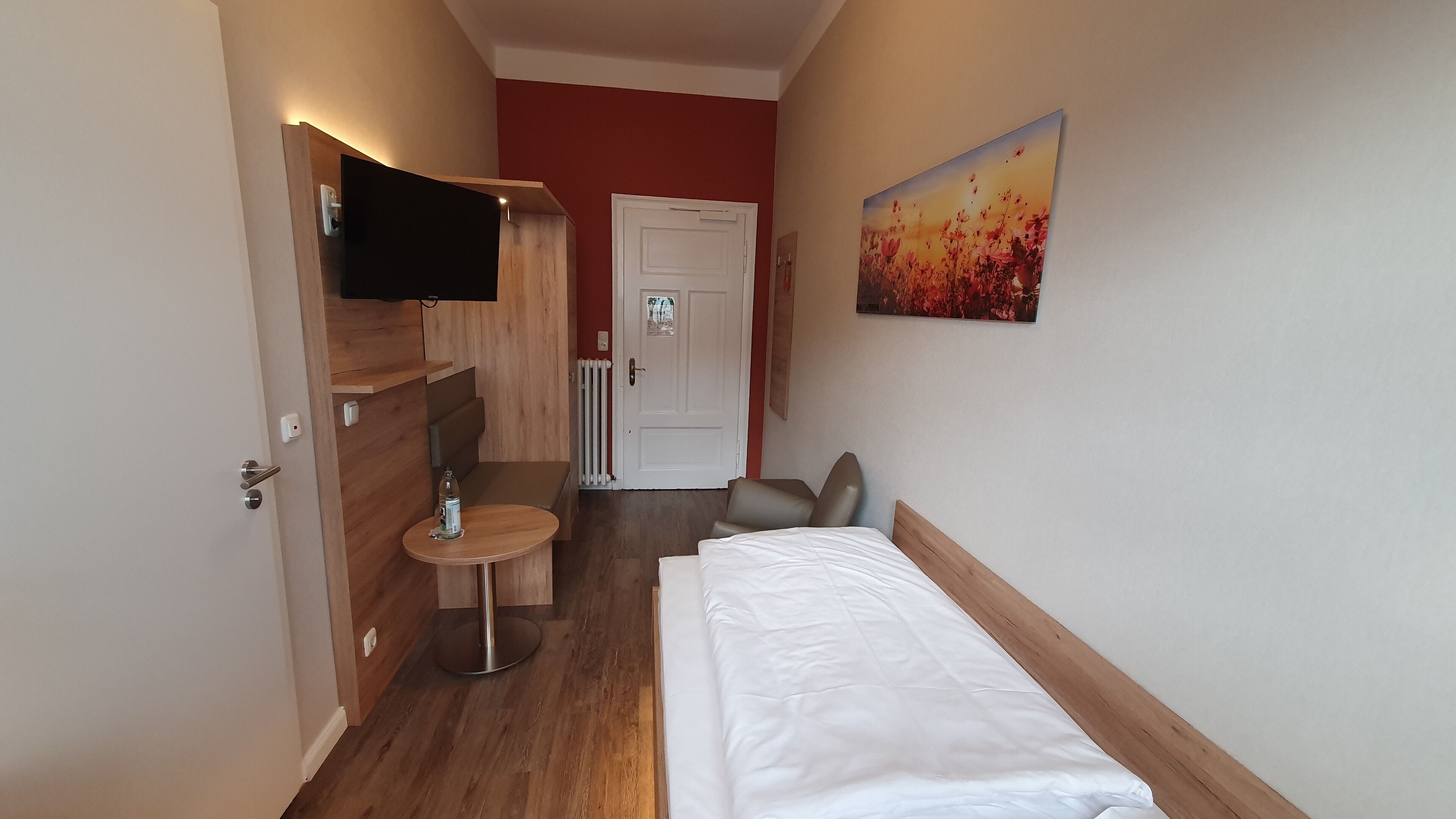 A hotel room with a bed, a small table, a TV, and a painting on the wall.