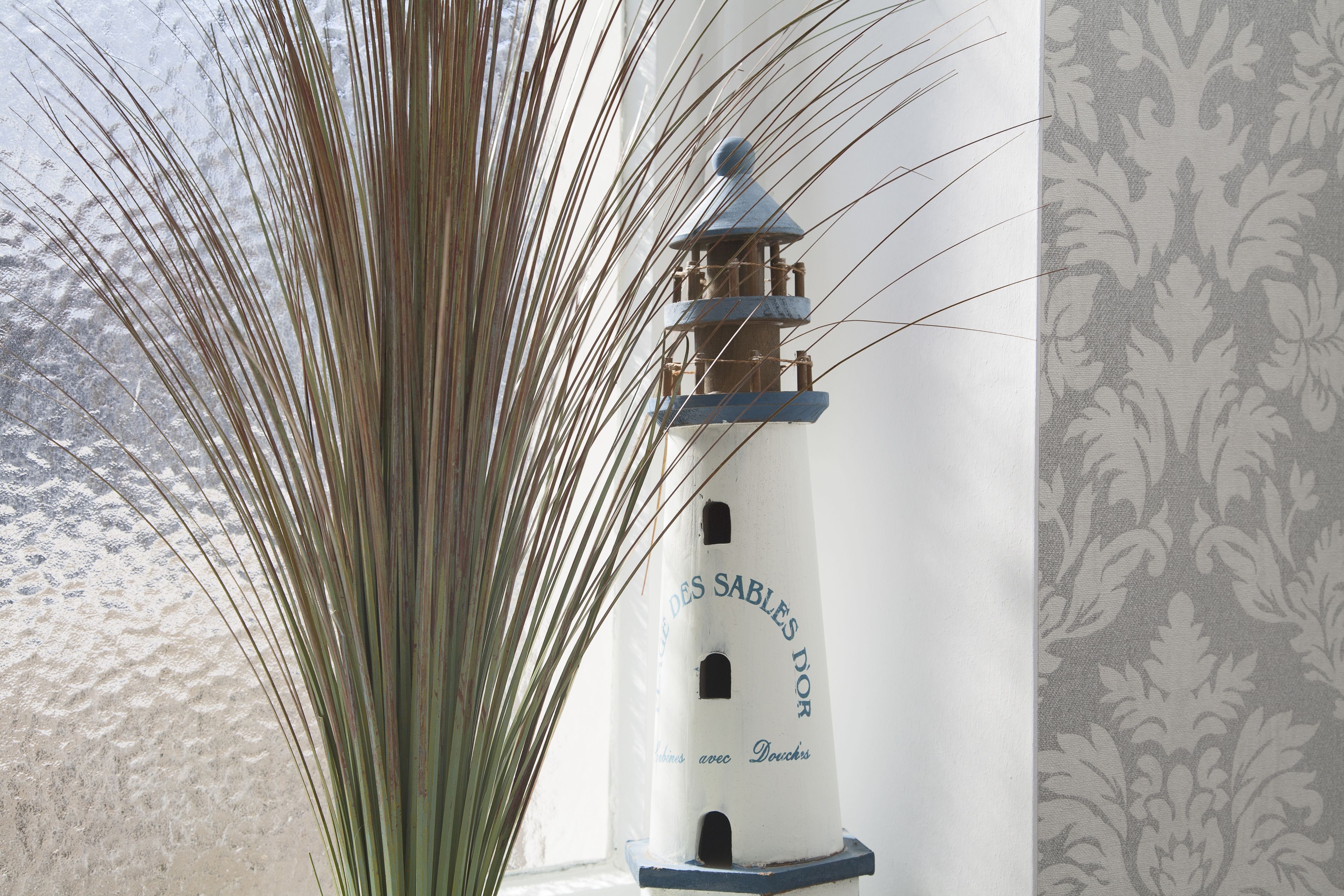 A lighthouse model with text on its side, positioned next to a window with a patterned curtain.