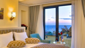Een hotelkamer met een groot bed, een stoel, een tafel met een kaars, en uitzicht op zee.