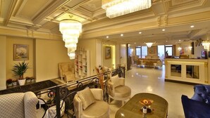 Een ruime lobby met een marmeren receptiebalie, een zithoek met banken en fauteuils, en een kroonluchter.