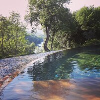 Un área de piscina tranquila al aire libre con vista despejada a un río y abundante vegetación.