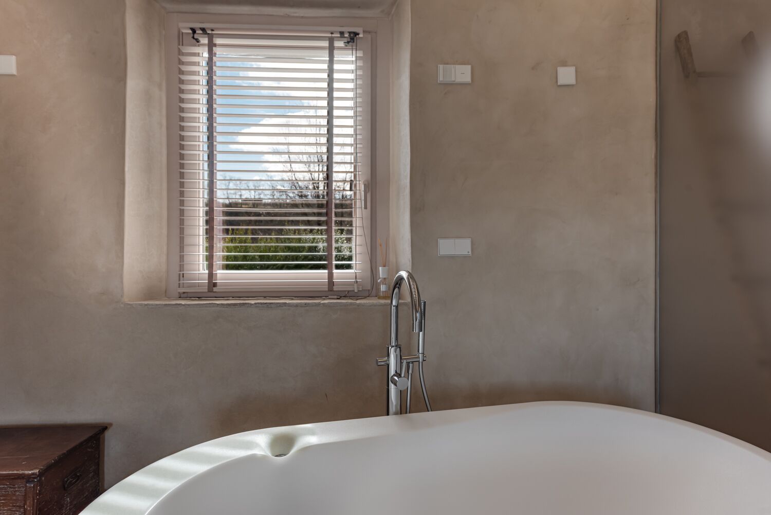 A bathroom with a bathtub, a window with blinds, and a shower area.