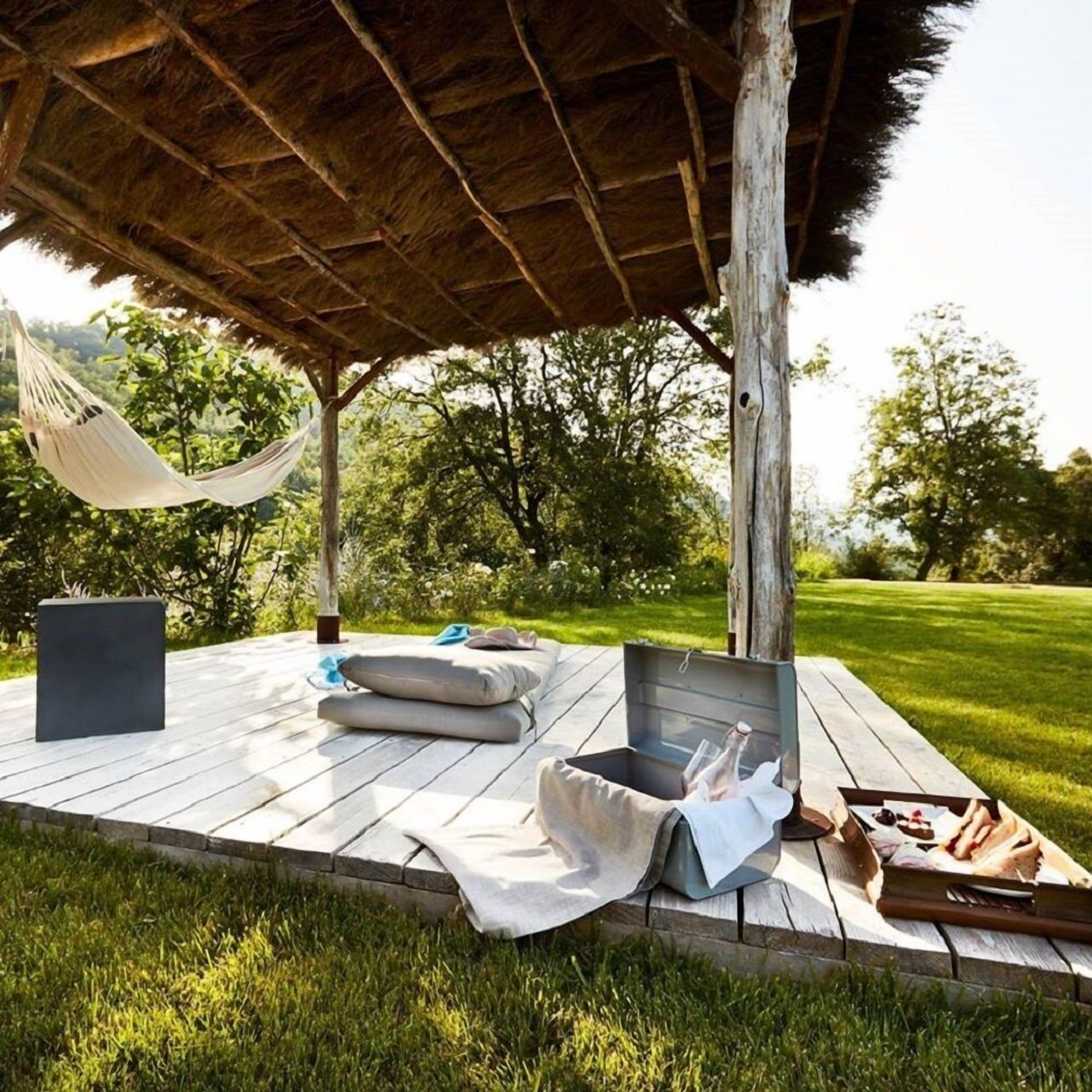 An outdoor seating area with a hammock, cushions, and a picnic setup.