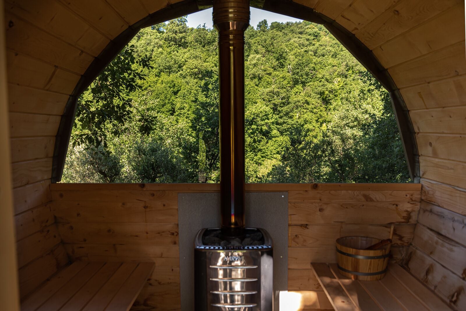 A wooden cabin with a large arched window overlooking a forest.
