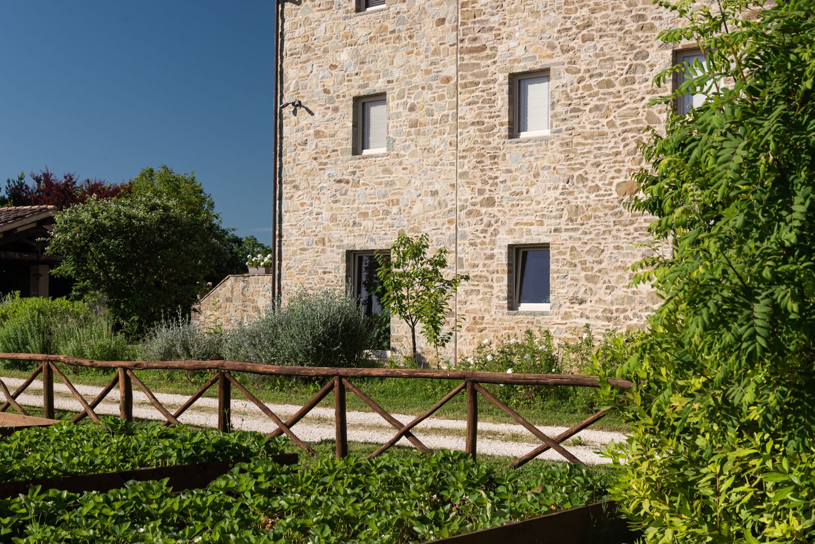 Un edificio in pietra con molte finestre, immerso nel verde e circondato da una recinzione di legno.
