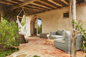 Un patio techado con mobiliario de mimbre, una hamaca colgante y piso de piedra.