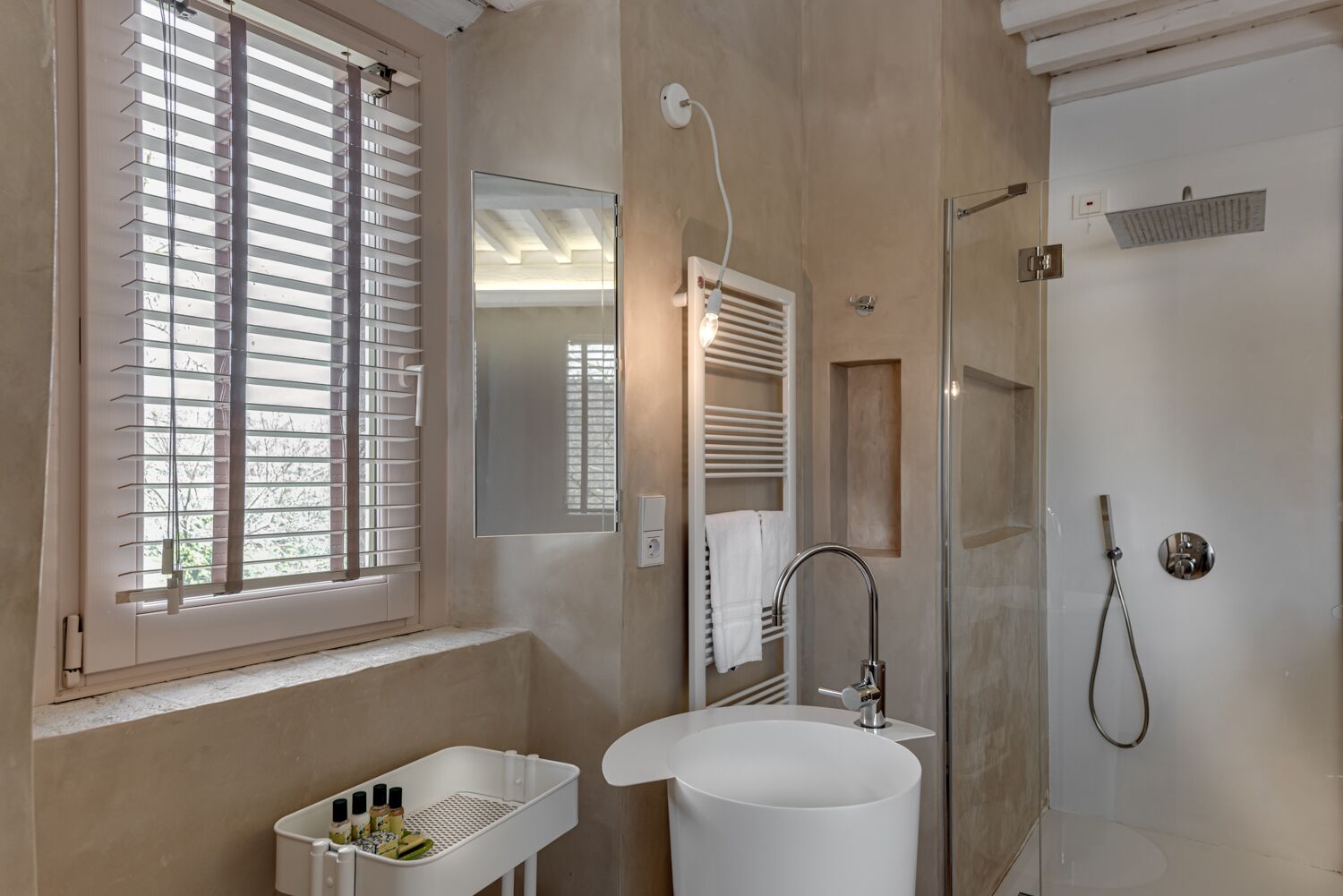 A modern bathroom with a large window, a white sink, a mirror, and a shower.