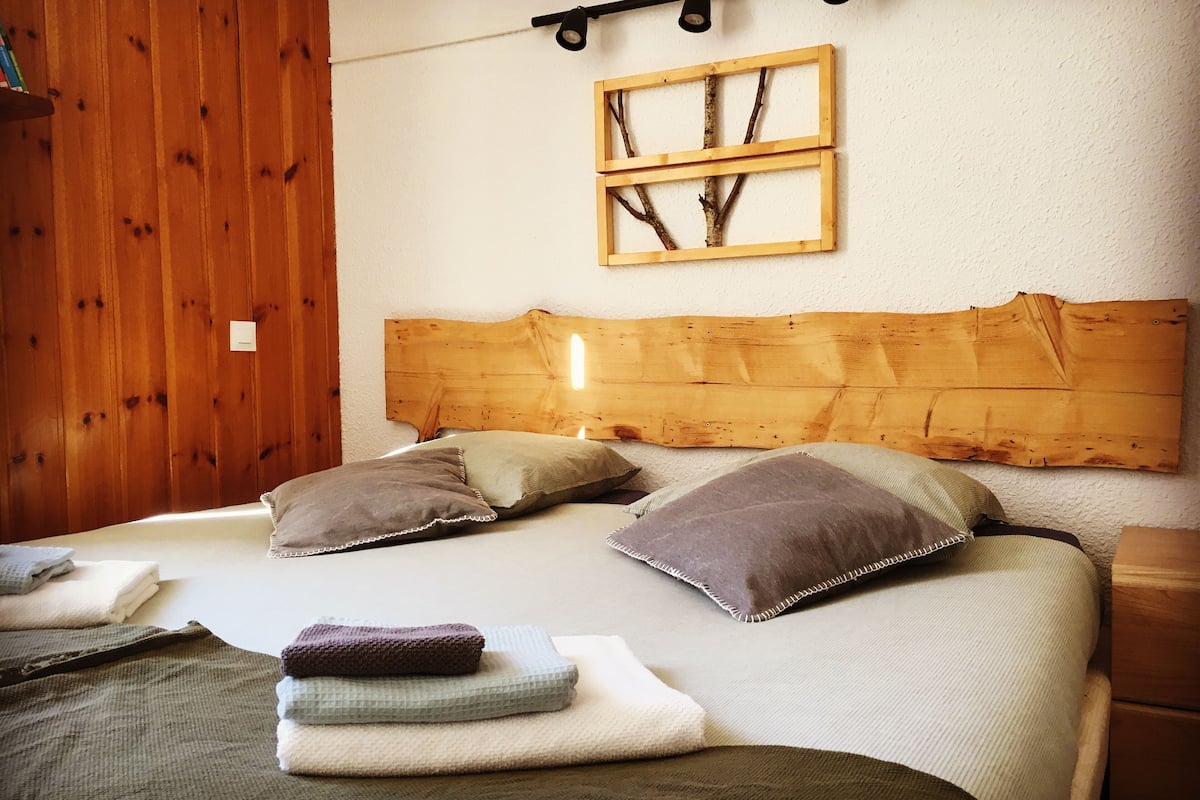 Una cama con cabecera de madera, varios almohadones y mantas dobladas.