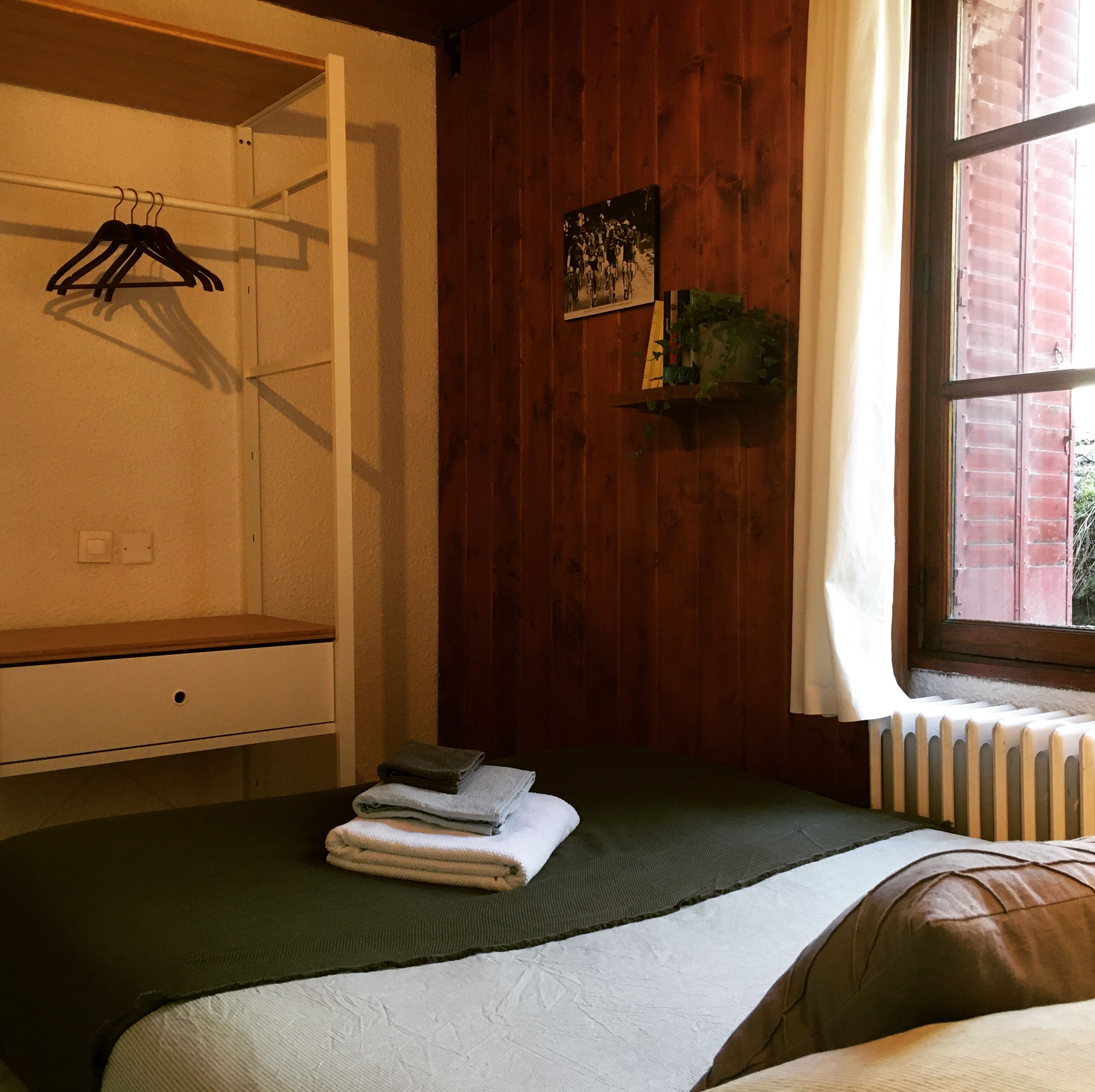 A room with a bed, a wooden wardrobe, a radiator, and a window with a curtain.